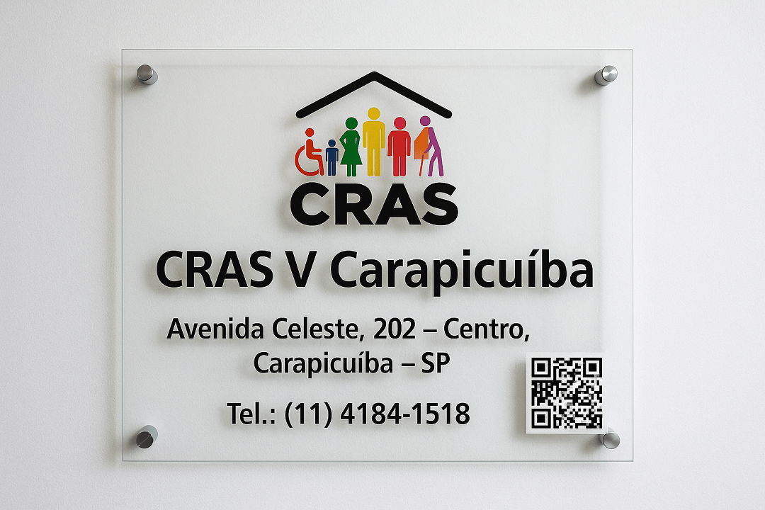Placa de vidro fixada na parede com o logotipo colorido do CRAS e os dizeres CRAS V Carapicuíba, Avenida Celeste, 202 – Centro, Carapicuíba – SP, com telefone de contato (11) 4184-1518 e QR Code para informações da unidade.